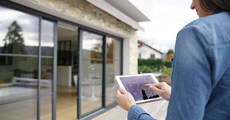 Une femme à l'extérieur d'une maison lance le système domotique sur sa tablette numérique