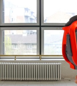 Main d’un homme pointant une caméra thermique vers le radiateur de chauffage et la fenêtre