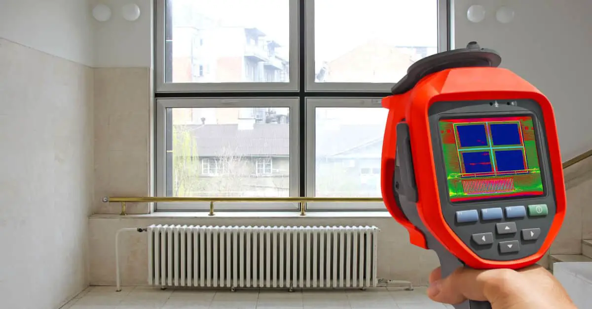 Main d’un homme pointant une caméra thermique vers le radiateur de chauffage et la fenêtre