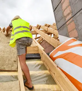 Un homme installant un matériau d'isolation de toit sur le toit d'une maison en construction