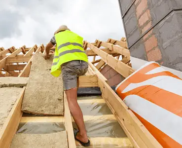 Un homme installant un matériau d'isolation de toit sur le toit d'une maison en construction