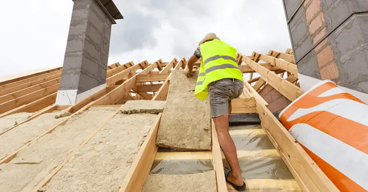 Un homme installant un matériau d'isolation de toit sur le toit d'une maison en construction