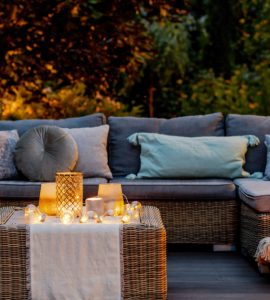 Un salon de jardin en rotin placé sur une terrasse en bois avec des luminaires allumés