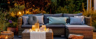 Un salon de jardin en rotin placé sur une terrasse en bois avec des luminaires allumés