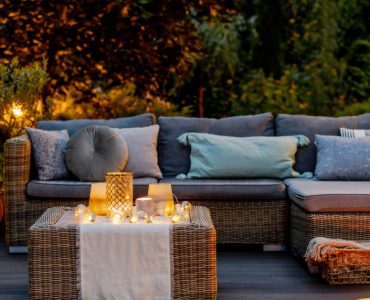 Un salon de jardin en rotin placé sur une terrasse en bois avec des luminaires allumés