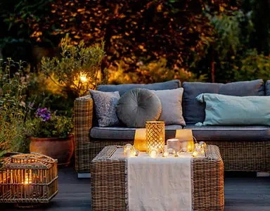 Un salon de jardin en rotin placé sur une terrasse en bois avec des luminaires allumés