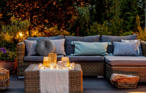 Un salon de jardin en rotin placé sur une terrasse en bois avec des luminaires allumés
