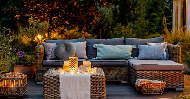 Un salon de jardin en rotin placé sur une terrasse en bois avec des luminaires allumés