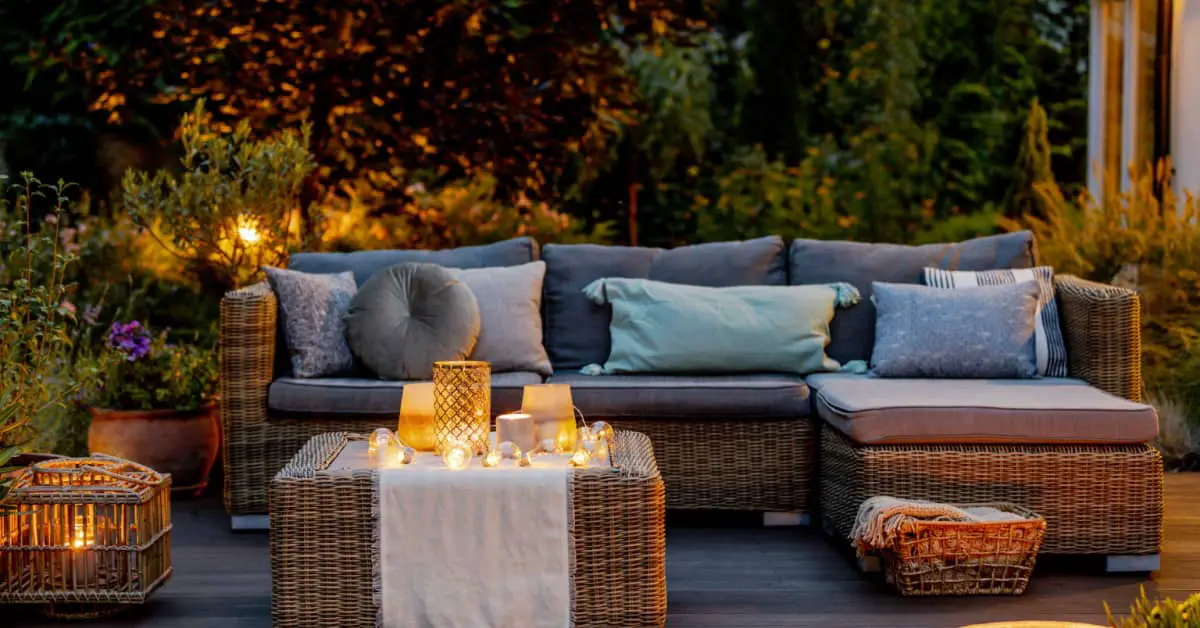 Un salon de jardin en rotin placé sur une terrasse en bois avec des luminaires allumés