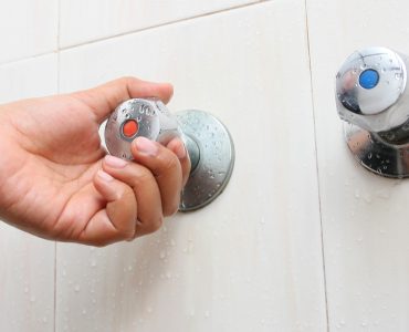 Main d'une femme tournant le robinet d'eau chaude dans la salle de bain