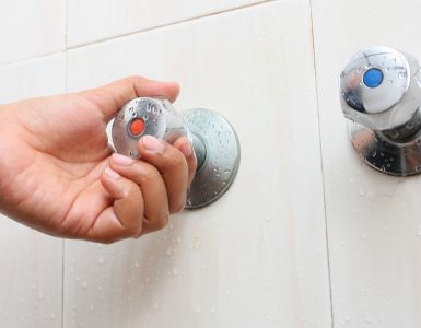 Main d'une femme tournant le robinet d'eau chaude dans la salle de bain
