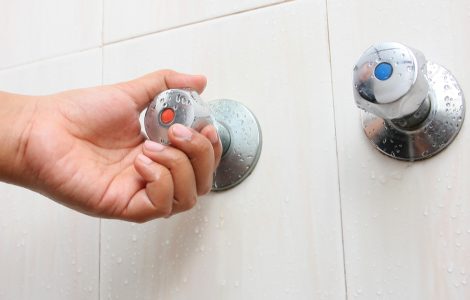 Main d'une femme tournant le robinet d'eau chaude dans la salle de bain