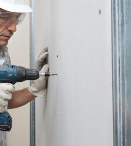 Un ouvrier en train de fixer une cloison avec sa perceuse visseuse