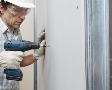 Un ouvrier en train de fixer une cloison avec sa perceuse visseuse
