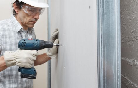 Un ouvrier en train de fixer une cloison avec sa perceuse visseuse