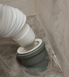 Un homme bougeant le siège de toilette pour relier le flexible à l'évacuation au sol