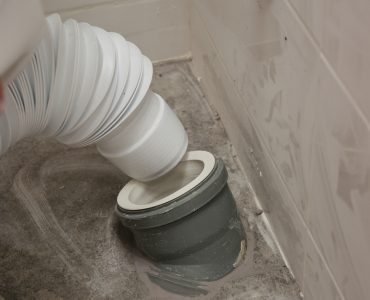 Un homme bougeant le siège de toilette pour relier le flexible à l'évacuation au sol