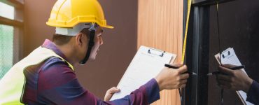 Un homme avec un casque de chantier prend des mesures de la porte vitrée