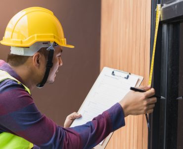 Un homme avec un casque de chantier prend des mesures de la porte vitrée