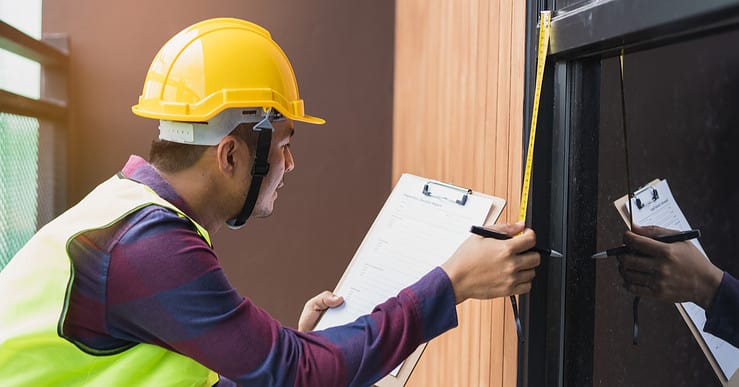 Un homme avec un casque de chantier prend des mesures de la porte vitrée