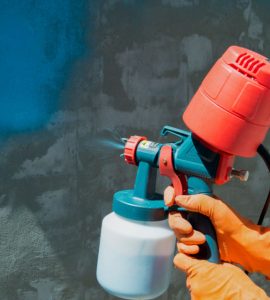 Un homme peint un mur en bleu à l’aide d’un pistolet à air
