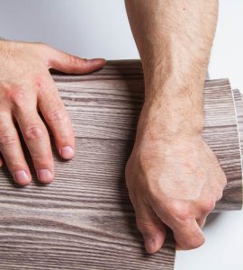 Zoom sur les mains d'un homme enroulant un rouleau de linoléum marron