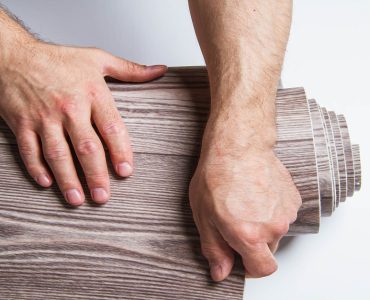 Zoom sur les mains d'un homme enroulant un rouleau de linoléum marron