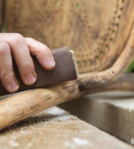 Zoom sur les mains d'un homme en train de poncer une chaise ancienne avec du papier de verre