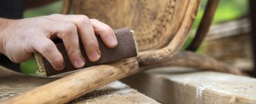 Zoom sur les mains d'un homme en train de poncer une chaise ancienne avec du papier de verre