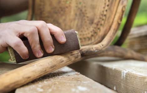 Zoom sur les mains d'un homme en train de poncer une chaise ancienne avec du papier de verre