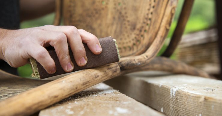 Zoom sur les mains d'un homme en train de poncer une chaise ancienne avec du papier de verre