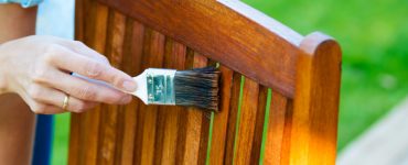 Zoom sur la main d’une femme appliquant du vernis sur une chaise de jardin en bois