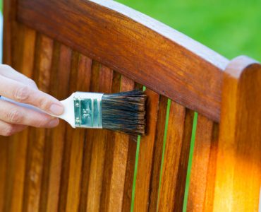 Zoom sur la main d’une femme appliquant du vernis sur une chaise de jardin en bois