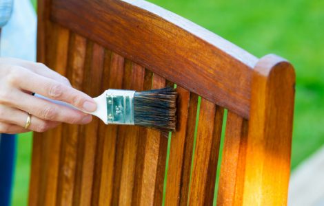 Zoom sur la main d’une femme appliquant du vernis sur une chaise de jardin en bois
