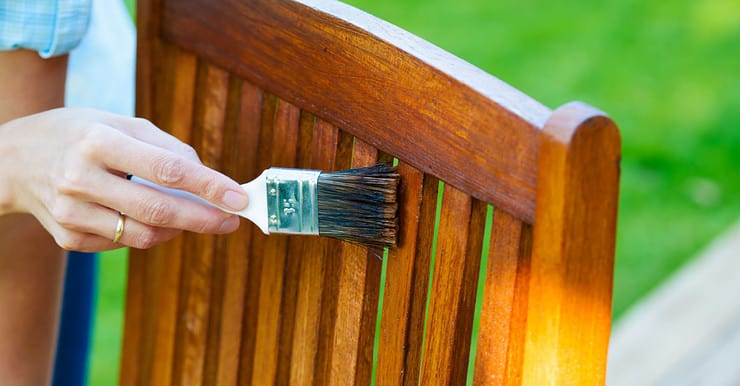 Zoom sur la main d’une femme appliquant du vernis sur une chaise de jardin en bois