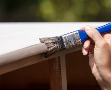 Zoom sur la main d'une femme peignant un vieux placard en bois en blanc