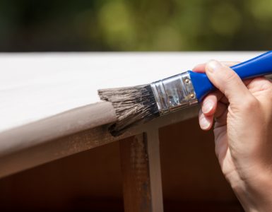 Zoom sur la main d'une femme peignant un vieux placard en bois en blanc