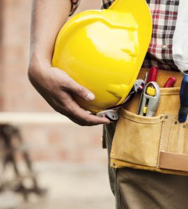 Un homme avec une ceinture porte-outils tient un casque de chantier jaune à la main