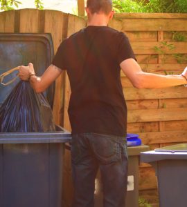 Un homme en train de déposer des déchets ménagers dans des bacs de recyclage différents
