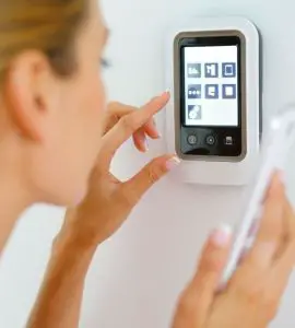 Une femme tenant un smartphone à la main touche l'interface d'une maison connectée