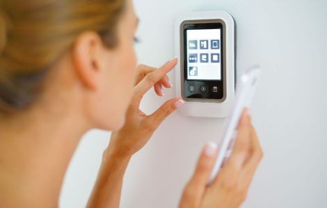 Une femme tenant un smartphone à la main touche l'interface d'une maison connectée