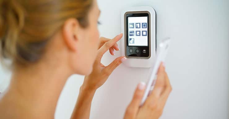 Une femme tenant un smartphone à la main touche l'interface d'une maison connectée