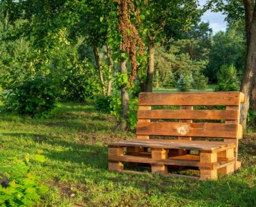 Une chaise en palettes au milieu d’un parc avec des arbres