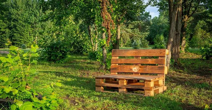 Une chaise en palettes au milieu d’un parc avec des arbres