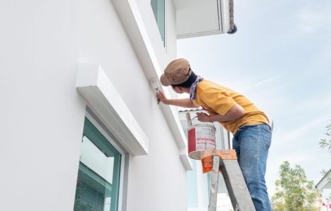 Une personne sur une échelle en train de peindre le mur extérieur avec un pinceau