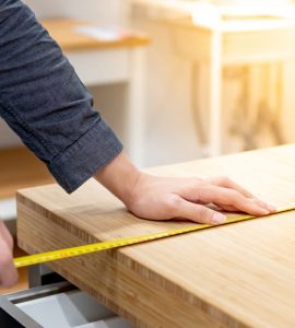 Zoom sur les mains d’un homme utilisant un mètre ruban pour mesurer une surface en bois