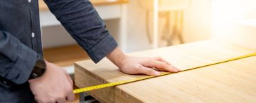Zoom sur les mains d’un homme utilisant un mètre ruban pour mesurer une surface en bois