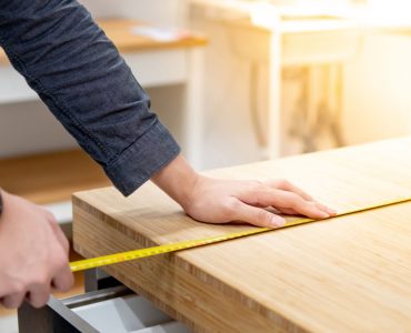 Zoom sur les mains d’un homme utilisant un mètre ruban pour mesurer une surface en bois