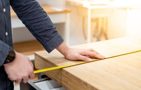 Zoom sur les mains d’un homme utilisant un mètre ruban pour mesurer une surface en bois