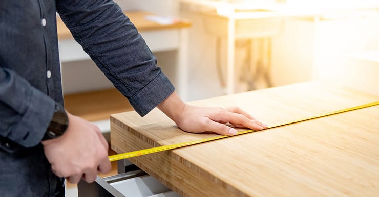 Zoom sur les mains d’un homme utilisant un mètre ruban pour mesurer une surface en bois